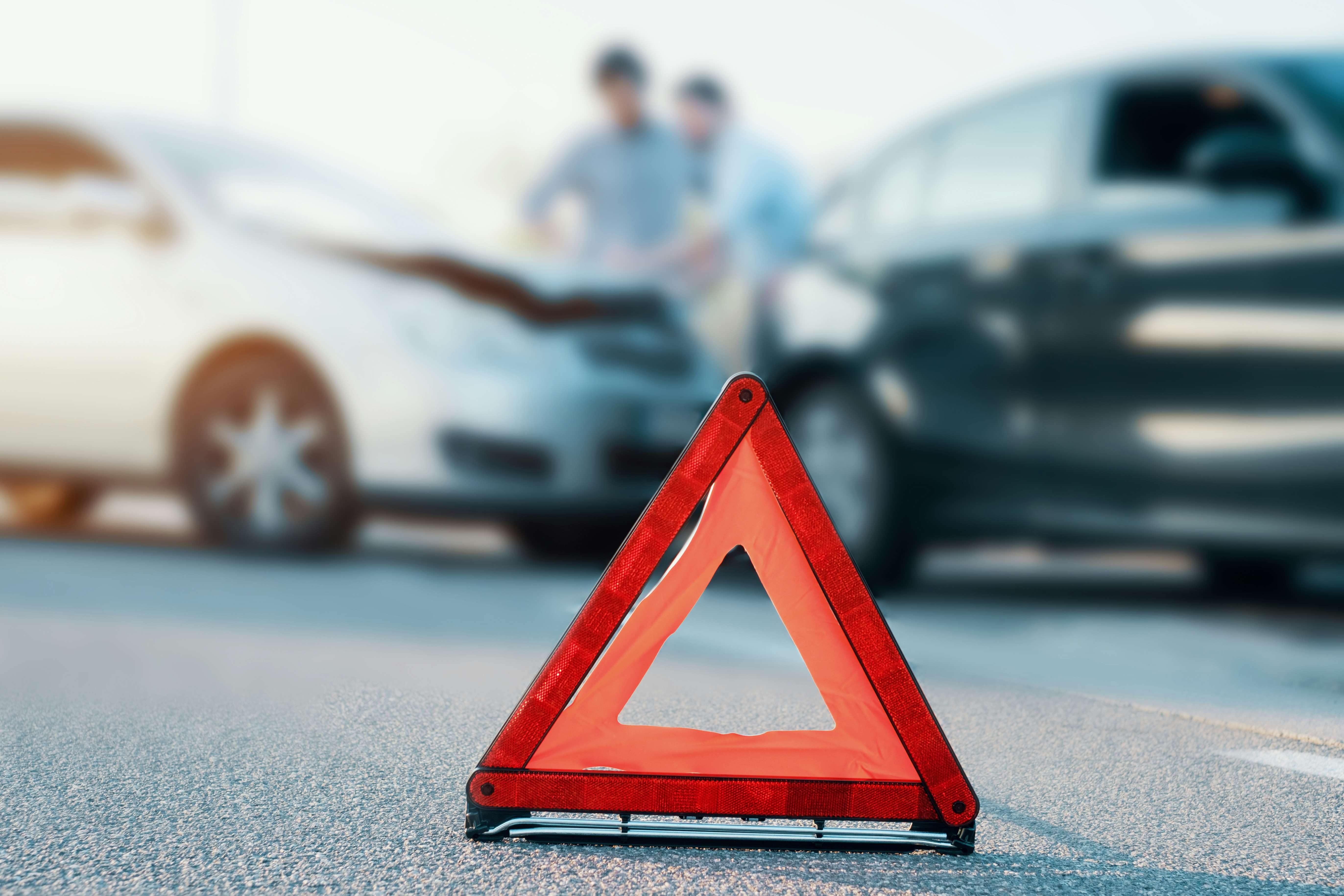 Two cars in the road following and accident or crash, red warning triangle in front of them