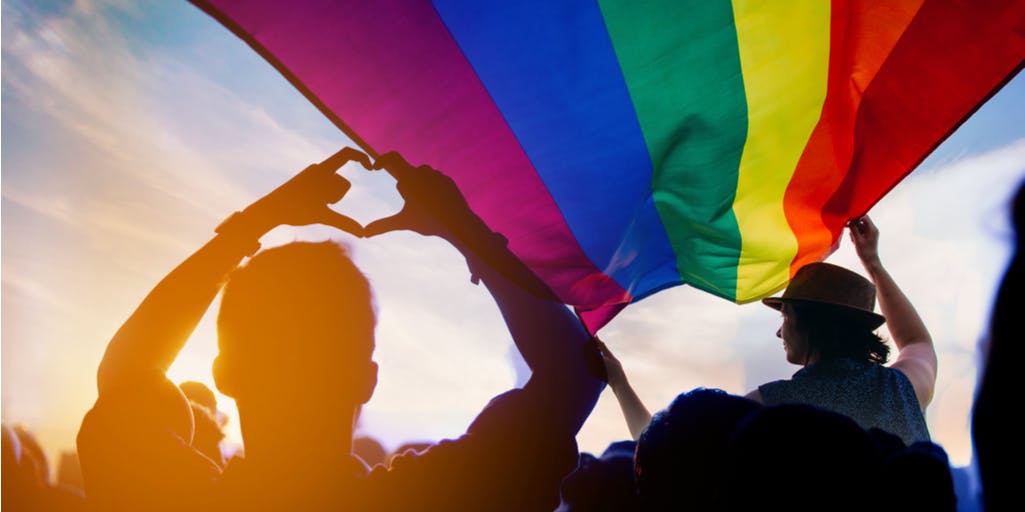 A picture of an LGBTQ+ flag with a crowd of people.