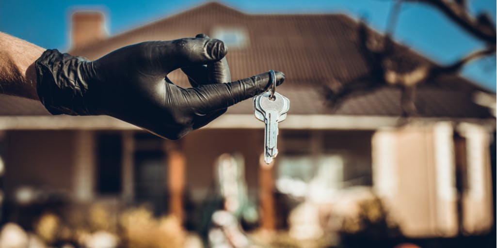 Photograph of a gloved hand holding keys in front of a house