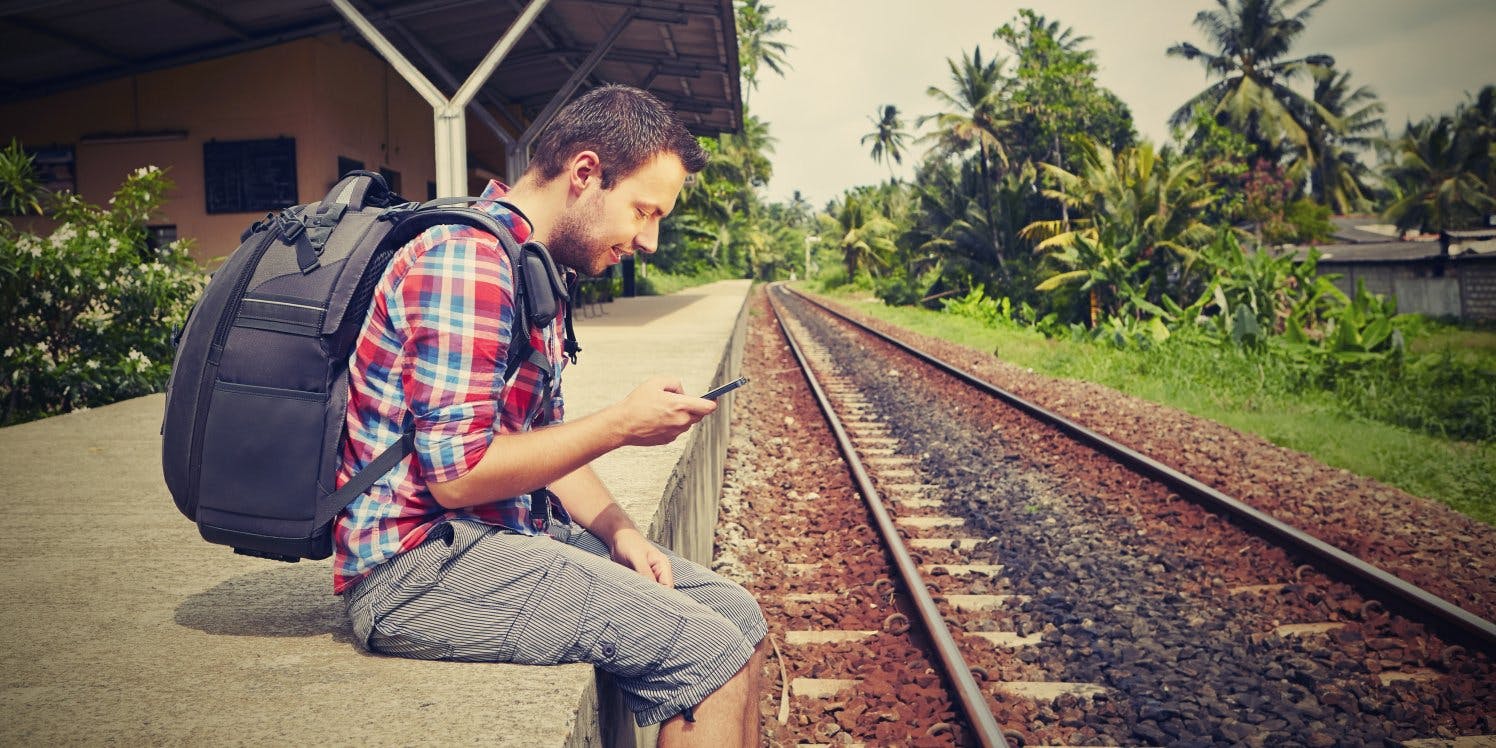 Young travel with backpack sitting by train tracks