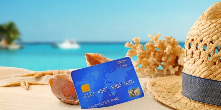 credit card on the beach by shells, coral and a hat