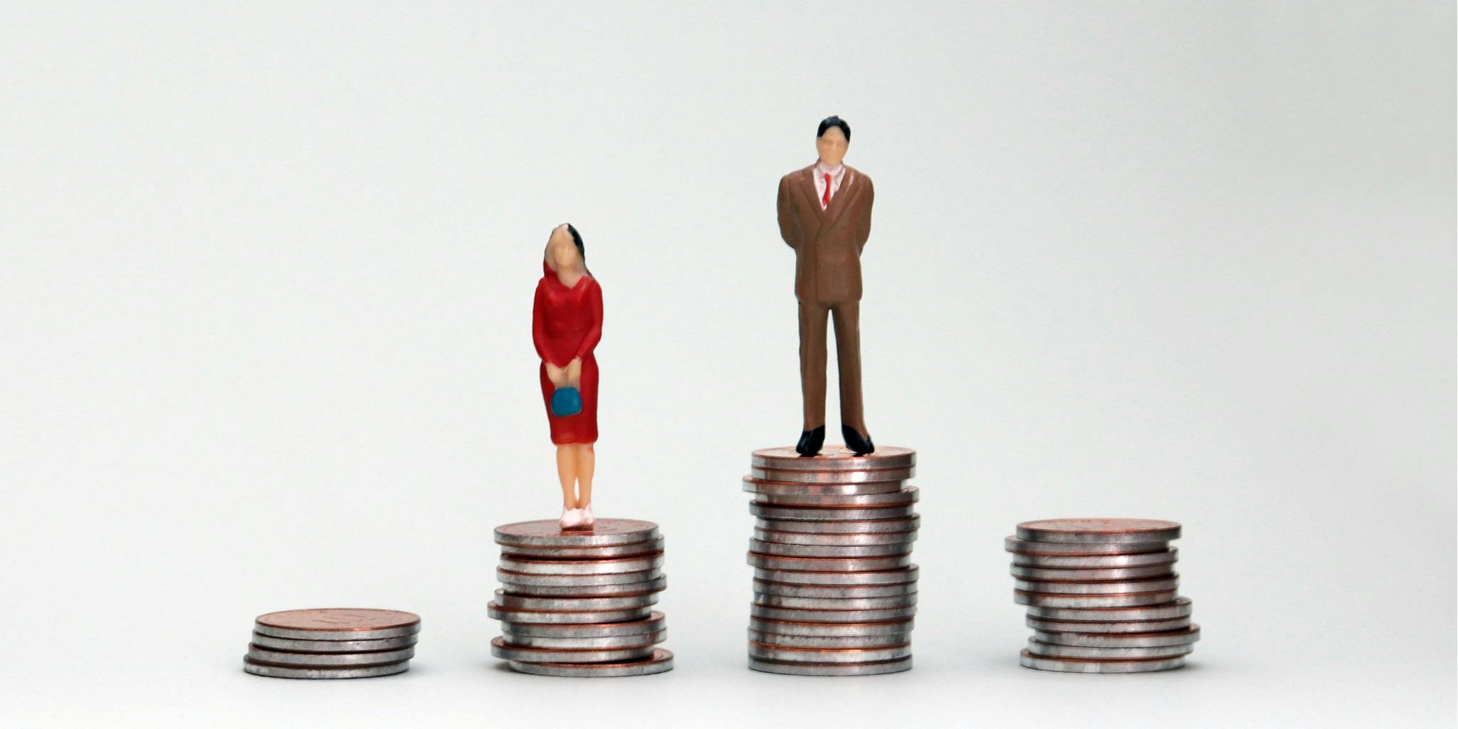 Gender wage difference concept. A miniature man and a woman standing on top of a pile of coins.