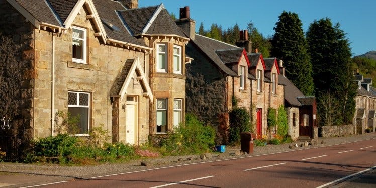 2 Scottish houses by a road. One house has a white door and the other has a red door.
