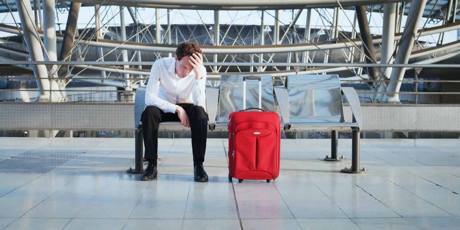Stressed man with luggage sitting on bench at airport
