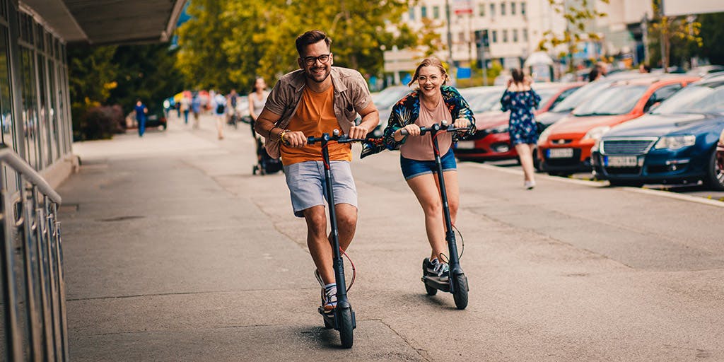 Young couple having fun driving electric scooters through the city.